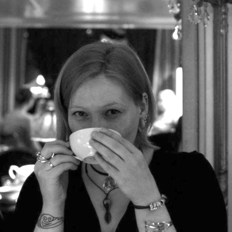 Foto von Klaudia Zotzmann-Koch in einem Café mit einer weißen Teetasse, aus der sie gerade trinkt
